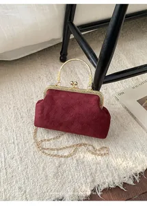 Detailansicht der dunkelroten Samtstruktur und des goldenen Metallgriffs der Handtasche