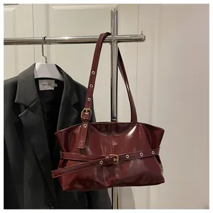 Close-up of wine red glossy oil wax leather handbag with golden adjustable buckle detail