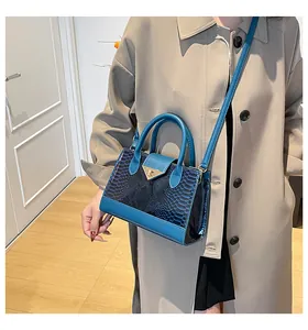 Dettaglio borsa blu motivo coccodrillo con chiusura dorata abbinata a un trench