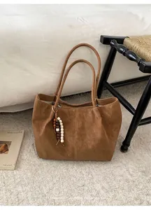 Close-up of brown suede tote bag with decorative stitching and wooden bead tassel