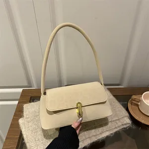 Minimalist beige suede shoulder bag with golden swivel lock on a soft wooden table