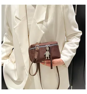 Detail showing deep brown crossbody camera bag with robot charm and silver hardware on model
