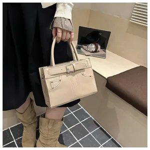 Detail of beige tote bag showing decorative belt buckle and rivet accents in a workspace