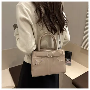 Beige tote bag with silver rivets and buckle detail shown on model in a modern interior