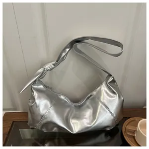 Detail of silver metallic underarm bag with knotted shoulder strap on wooden table