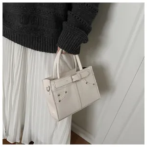 Detail view of cream white PU leather tote bag with silver rivets and buckle straps