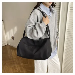 Detail of a black nylon travel bag with front zipper shown worn by a model in a minimalist room