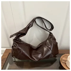 Detail of a deep brown faux leather knotted shoulder bag on a minimalist wooden table