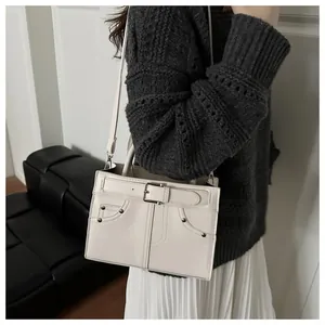 Close-up of white shoulder bag with decorative belt buckle and metal rivets on model