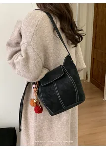 Détail du sac seau noir minimaliste avec coutures contrastées blanches et pompons décoratifs