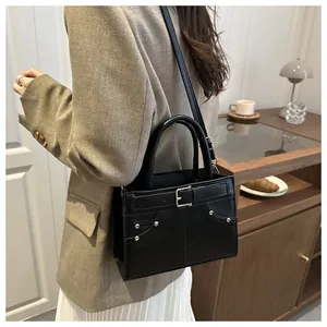 Black tote bag with silver rivets and decorative buckle strap worn by a model
