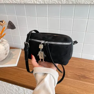 Black minimalist crossbody bag with suede finish and silver robot pendant on a wood surface