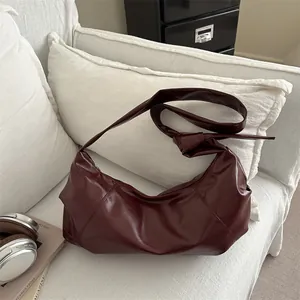 Burgundy faux leather half-moon crossbody bag with knot strap on white fabric sofa