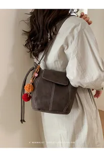 Vue détaillée d'un sac seau en daim marron foncé avec pompons colorés et coutures fines