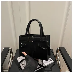 Detail of matte black leather tote featuring decorative straps, rivets and sturdy handles