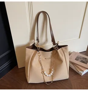Dettaglio della borsa tote beige e marrone con catena dorata e ciondolo di perle