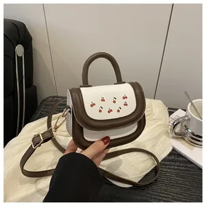 Detail of crossbody bag featuring red cherry print and premium gold-tone hardware finish