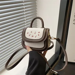 Mini cherry print crossbody bag with cream body and dark brown trim accents