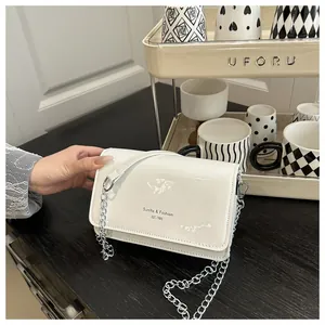 Detail van de witte glanzende schoudertas met zilveren ketting en logoklep