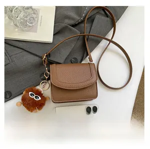 Detailed close-up of brown litchi grain leather bag with a cute pom-pom charm