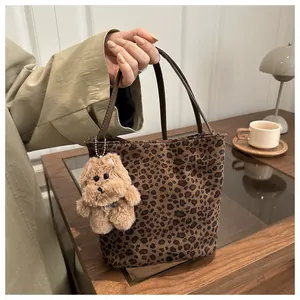 Detail van luipaardprint bucket bag met pluche hondenbedeltje op een houten bureau