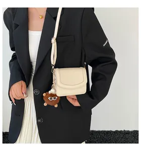 Chic cream litchi texture crossbody bag with adjustable strap and cute plush monster charm