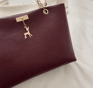 Gros plan du sac cabas bordeaux avec pendentif cerf doré et détails de chaîne