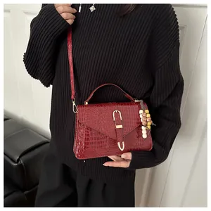 Detail of dark red croc-embossed leather handbag with gold buckle and beaded charm