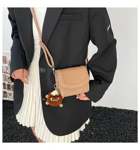 Detail of beige faux leather crossbody bag with a brown plush monster charm accessory