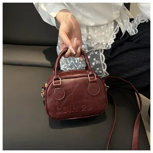 Detail of burgundy shell bag with embossed letters and adjustable leather shoulder strap