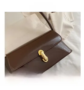 Close-up of glossy brown baguette bag featuring a shiny gold oval clasp and patent texture