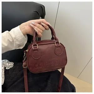Detail of burgundy shell bag with embossed letters and adjustable crossbody strap
