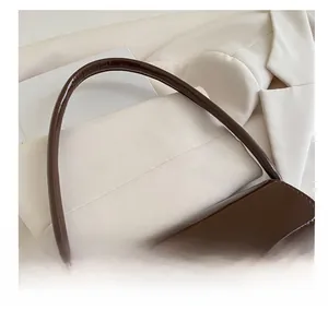 Detail of dark brown glossy patent leather texture and gold metal clasp on baguette bag