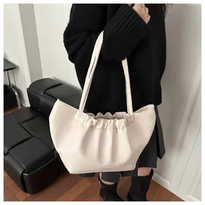 Chic cream leather tote bag with pleated cloud top design worn on shoulder