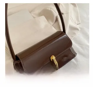 Detail of a dark brown patent leather baguette bag with a gold twist lock and shoulder strap