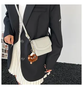 Detail of off-white crossbody bag featuring pebbled texture and a cute brown plush pendant