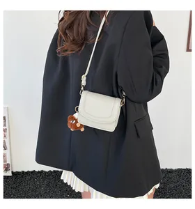 Detail of cream-white shoulder bag worn with a black blazer and brown plush charm