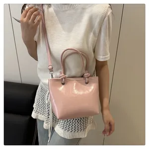 Detail van roze laksleren tas met glanzende textuur en dubbele handvatten met riem