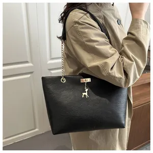 Close-up of black matte tote bag featuring a gold deer pendant and elegant chain strap