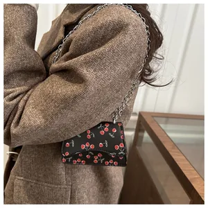Detailansicht der Mini-Umhängetasche in Schwarz mit Kirschmuster auf der Schulter des Models