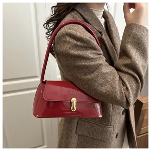 Side view of red patent leather baguette bag with gold buckle on shoulder