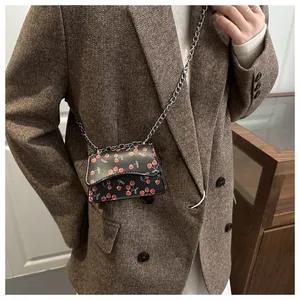 Detailansicht der Mini-Umhängetasche mit Kirschmuster und Silberkette auf Blazer