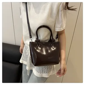 Detail van een glanzende donkerbruine mini tote bag met geknoopte riemdetails op een model
