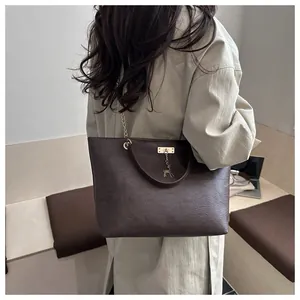Detail of dark brown leather tote bag showing grainy texture and golden deer charm accent