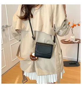 Detailed back view of a black textured crossbody bag with brown plush charm on a model
