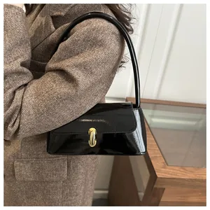 Detail of a black patent leather baguette bag with a gold buckle on a model in a blazer
