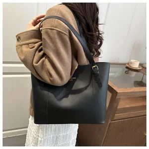 Detail of minimalist black tote bag with gold lettering shown on model's shoulder