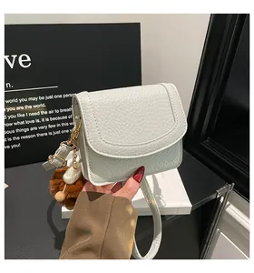 Close-up of white lychee grain leather bag with gold buckle and brown plush charm