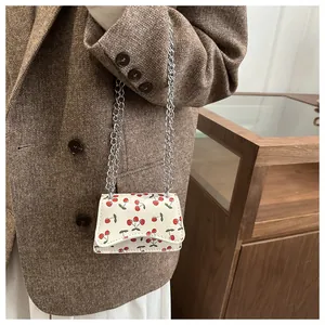 Detail einer weißen Mini-Kettentasche mit Kirschprint an einem Model im braunen Blazer