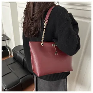 Detail of burgundy leather tote bag featuring a gold chain strap and deer pendant charm